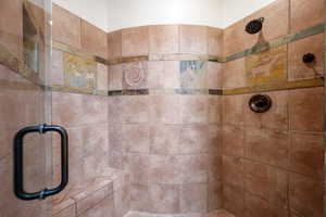 Enclosed shower featuring a tiled bench seat, bronze fixtures, decorative accent tiles, a glass enclosure, and a built-in shower niche