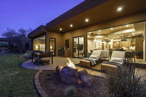 Patio terrace at dusk with an outdoor kitchen, an outdoor fire pit, an outdoor living / dining area, a patio area, and a lawn