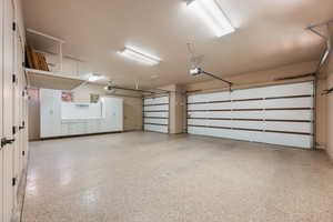 Spacious garage featuring a speckled epoxy floor, multiple white storage cabinets with a workbench, two automatic garage door openers, overhead storage racks, and fluorescent lighting