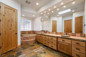 Spacious bathroom featuring a built-in soaking tub with tiled surround, a long double vanity with stone-finish countertop, and slate-finish flooring