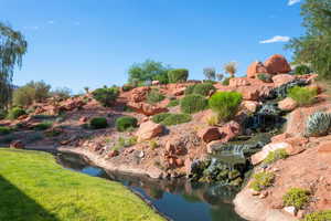 Landscaped backyard featuring a tiered waterfall, a natural stream, a manicured grass area, desert vegetation, and large rock formations