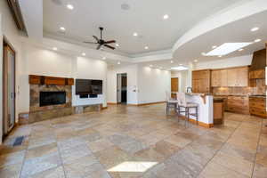 Open-concept living area featuring large format tile flooring, a stone-clad fireplace, and a kitchen with wood cabinetry and an island with counter seating