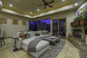 Living room with a raised ceiling, ceiling fan, recessed lighting, and a stone fireplace