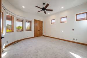 Carpeted room with a ceiling fan, recessed lighting, and multiple windows