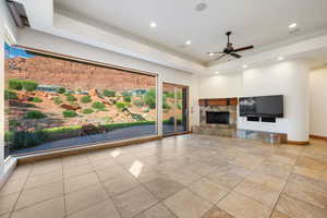 Spacious living area featuring a large picture window, stone-clad fireplace with wood mantel, tile flooring, recessed lighting, and a ceiling fan