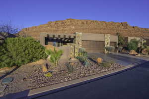 View of front of property featuring an attached garage, a mountain view, stone siding, driveway, and stucco siding