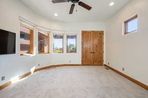 Carpeted room with a curved wall featuring multiple windows, recessed lighting, and a ceiling fan