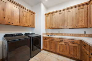 Laundry room featuring extensive wood cabinetry, a built-in sink with a gooseneck faucet, tile countertops, and a decorative tile backsplash