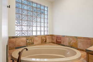 Soaking tub with a bronze-finish faucet, surrounded by decorative tile work and a glass block window