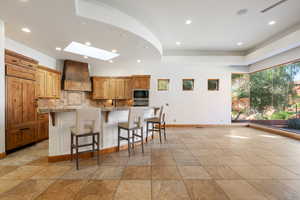 Spacious open-concept area featuring a kitchen island with seating, natural wood cabinetry, recessed lighting, and a skylight