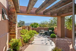 Covered patio featuring exposed wood beams, stacked stone accents, a concrete pathway, and landscaped gravel beds