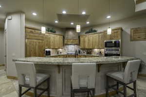 Kitchen with a breakfast bar area, light wood finish cabinetry, light stone countertops, decorative backsplash, and stainless steel appliances