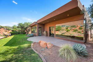 Contemporary stucco exterior with a covered patio, expansive glass windows, built-in outdoor grill, desert landscaping, and a manicured lawn