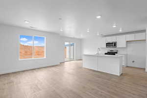 Kitchen with white cabinets, stainless steel appliances, a center island with sink, light wood-style flooring, and open floor plan