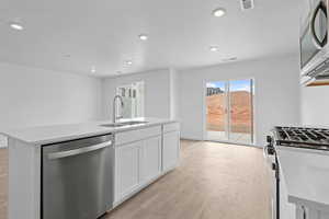 Kitchen with stainless steel appliances, white cabinetry, a center island with sink, light wood finished floors, and recessed lighting