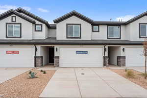 View of front of home with stucco siding, stone siding, an attached garage, concrete driveway, and a tiled roof