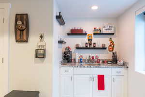 Indoor wet bar with light stone counters, white cabinets, and open shelves