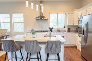 Kitchen with stainless steel appliances, hanging light fixtures, white cabinets, light wood-style flooring, and light stone counters