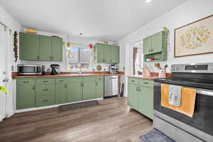 Kitchen with stainless steel appliances, green cabinets, open shelves, dark wood-type flooring, and butcher block countertops