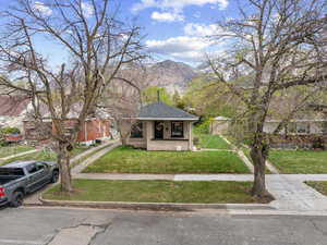 Bungalow-style home with covered porch, a front yard, a mountain view, roof with shingles, and brick siding