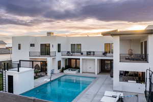 Rear view of property featuring stucco siding, a patio area, a balcony, and a pool with connected hot tub