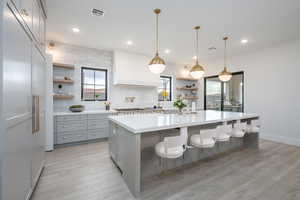 Kitchen with open shelves, backsplash, light wood-type flooring, a spacious island, and hanging light fixtures