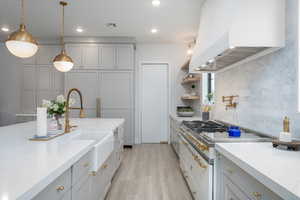 Kitchen featuring gray cabinets, light stone counters, hanging light fixtures, and light wood-style floors