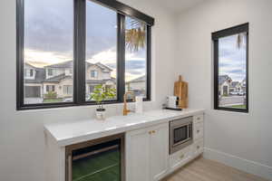 Kitchen with wine cooler, stainless steel microwave, light stone counters, and white cabinets