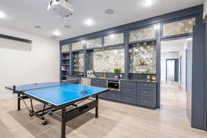Rec room with bar with sink, light wood finished floors, and recessed lighting