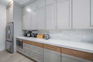 Dual tone kitchen featuring stainless steel appliances, light stone countertops, light wood finished floors, decorative backsplash, and two tone cabinetry