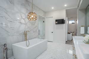 Bathroom with double vanity, tile walls, a freestanding tub, recessed lighting, and a stall shower