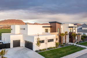 Contemporary house featuring a garage, driveway, stucco siding, a front yard, and a chimney