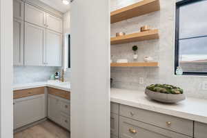 Kitchen featuring gray cabinets, open shelves, tasteful backsplash, and light wood-style floors