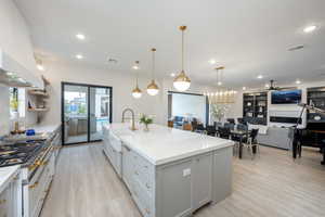 Kitchen with light stone counters, a spacious island, light wood finished floors, open floor plan, and gray cabinets