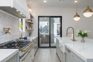 Kitchen with light stone counters, pendant lighting, open shelves, gray cabinets, and tasteful backsplash