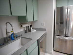 Kitchen with stainless steel appliances, green cabinetry, and light stone countertops