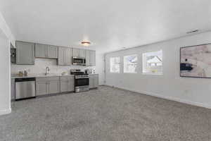 Kitchen featuring gray cabinets, stainless steel appliances, light countertops, and dark colored carpet