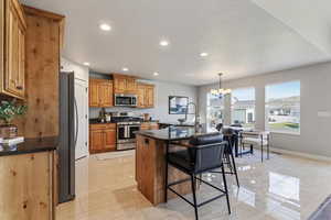 Kitchen featuring a kitchen island with sink, stainless steel appliances, hanging lights, and wood finish cabinets