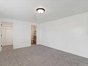 Unfurnished bedroom featuring a spacious closet, carpet floors, and ensuite bath