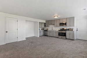 Kitchen with stainless steel appliances, dark colored carpet, light countertops, and gray cabinets