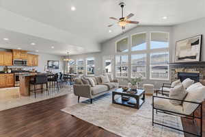 Living area featuring ceiling fan, dark wood-type flooring, a fireplace, hanging lights, and lofted ceiling