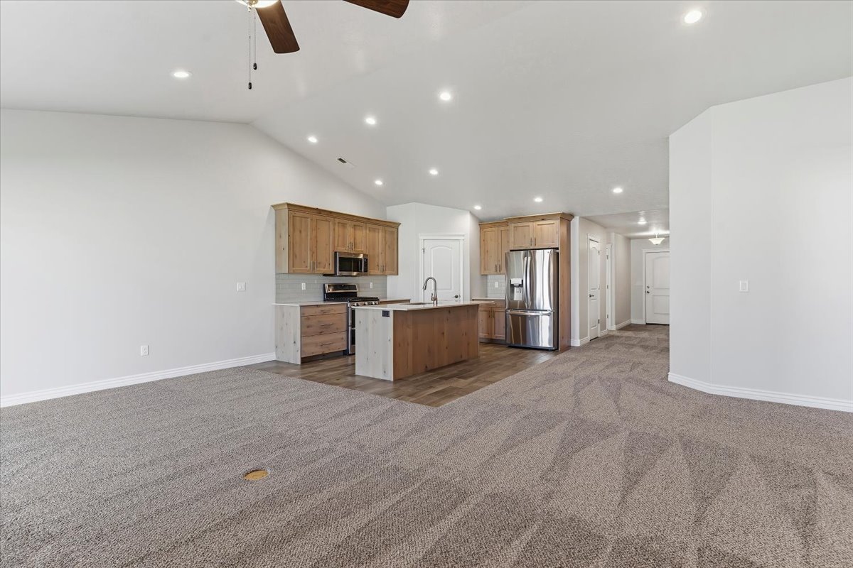 Kitchen featuring open floor plan, stainless steel appliances, dark colored carpet, a center island with sink, and ceiling fan