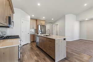 Kitchen featuring stainless steel appliances, tasteful backsplash, a center island with sink, wood tiled floors, and recessed lighting