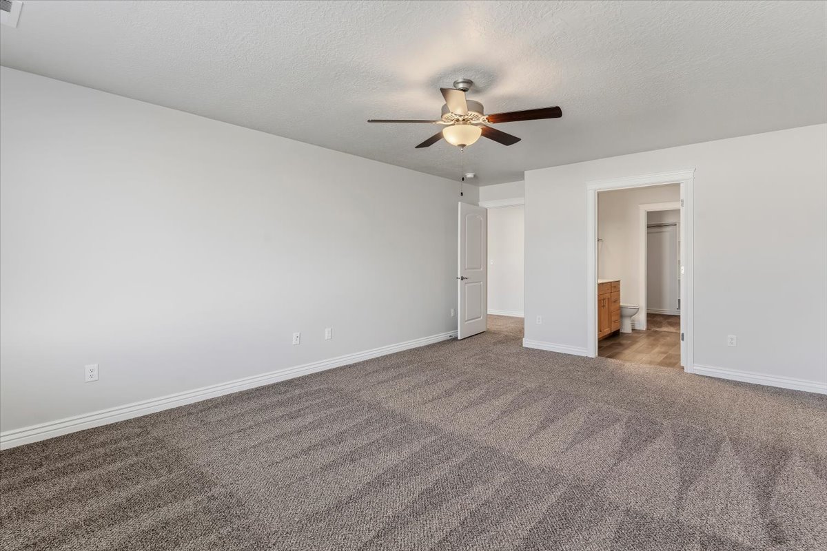 Unfurnished bedroom with ensuite bath, a ceiling fan, carpet floors, and a textured ceiling