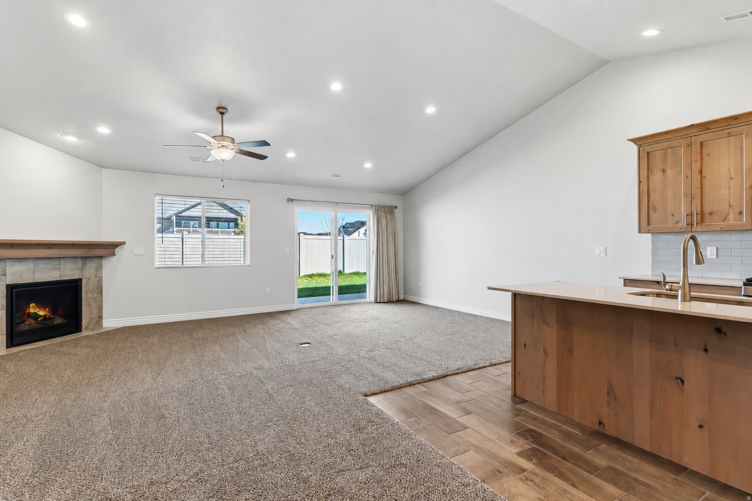Open-concept living space with vaulted ceilings, recessed lighting, and a stone-clad fireplace with a wood mantel