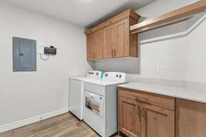 Laundry room featuring electric panel, wood tiled floors, cabinet space, and independent washer and dryer