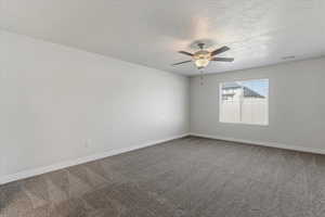 Unfurnished room featuring dark carpet, a ceiling fan, and a textured ceiling