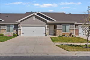 View of front facade featuring stone siding, an attached garage, concrete driveway, a front lawn, and stucco siding