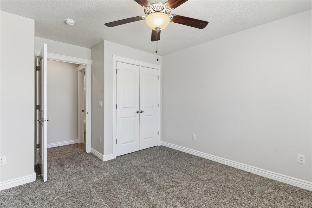 Unfurnished bedroom featuring a textured ceiling, dark colored carpet, a closet, and a ceiling fan