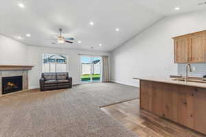 Unfurnished living room with light wood-type flooring, a fireplace, a ceiling fan, vaulted ceiling, and light colored carpet